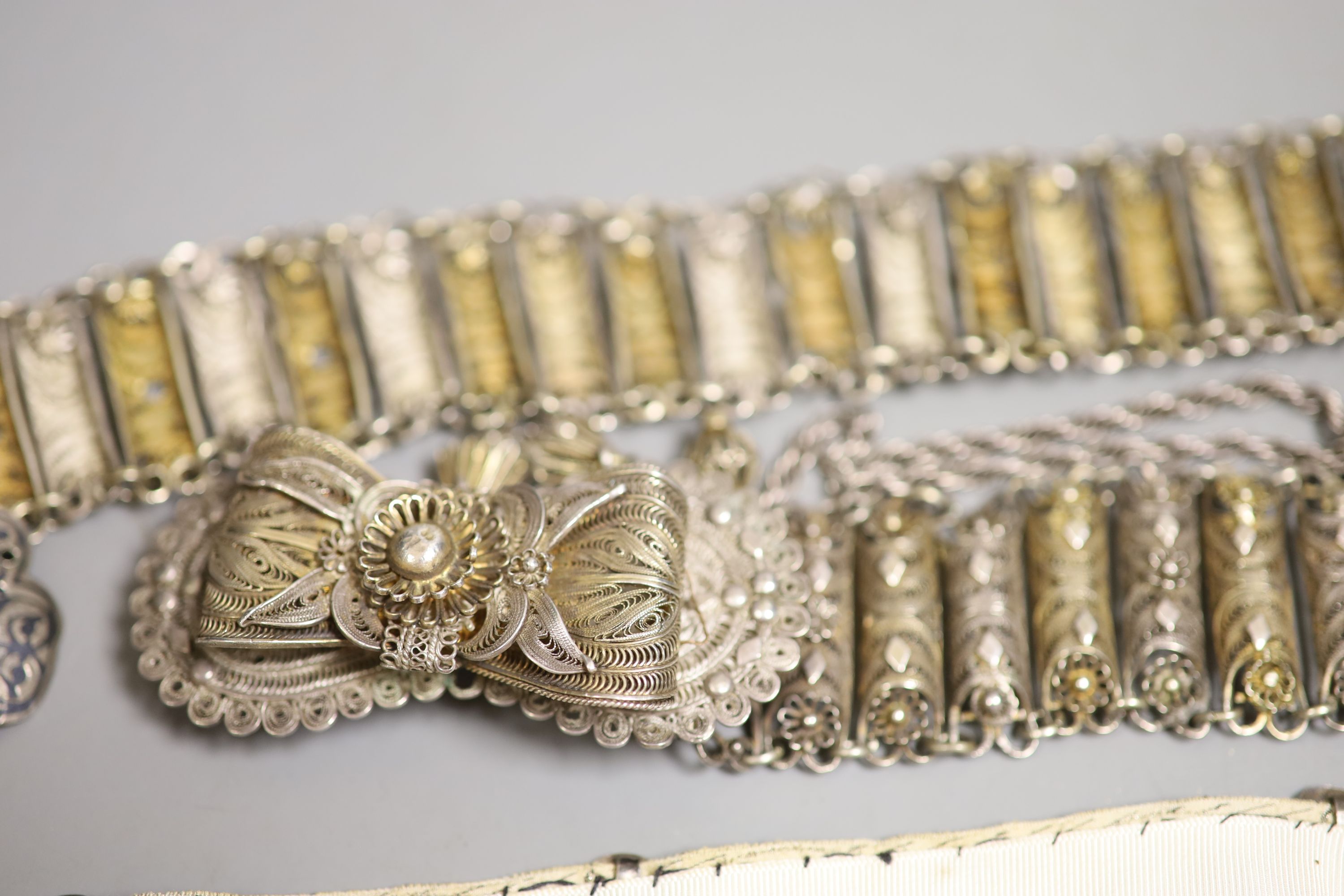 A white metal and niello belt buckle, one other on a sash belt and a filigree white metal belt.